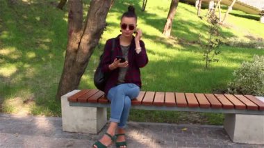 Genç güzel kız bir bankta otururken smartphone, şarkı söyler ve dans müzik dinlemek.