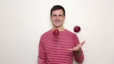 Çizgili kazaklı genç yakışıklı adam üç kırmızı elma ile juggles.