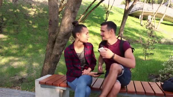 情侣们在智能手机上互相展示照片 坐在公园的长椅上 — 图库视频影像