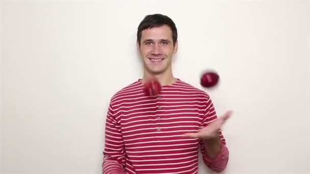 Młody przystojny facet w paski sweter żongluje trzy czerwone jabłka. — Wideo stockowe