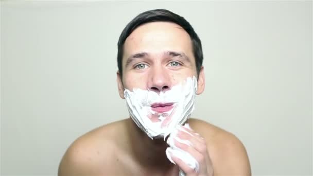 Joven chico guapo aplica espuma de afeitar y sonrisas . — Vídeos de Stock