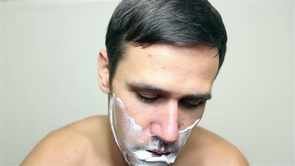 若いハンサムな男は かみそりで顔を剃る 白い背景の上の肖像画 — ストック動画