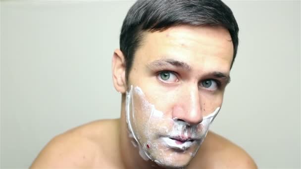 Νέων όμορφος άντρας ξυρίζει το πρόσωπό του με ένα ξυράφι. — Αρχείο Βίντεο