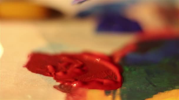 Artist lowers the brush in red paint and mixes it on the palette. — Stock Video