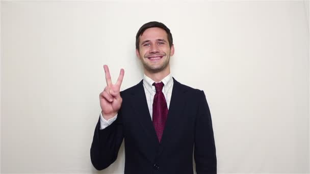 Jovem empresário bonito está sorrindo e mostrando gesto de vitória . — Vídeo de Stock