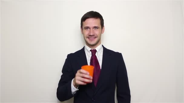 Joven hombre de negocios guapo bebe alcohol de una taza naranja . — Vídeos de Stock