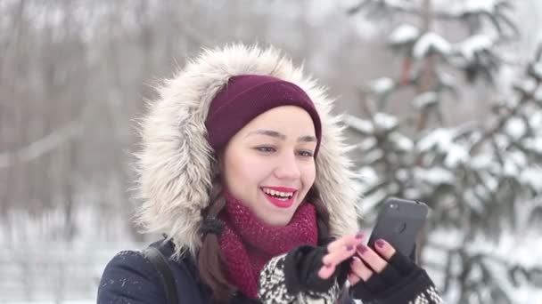 Belle jeune fille est activement retourner à travers le flux de nouvelles sur son smartphone tout en marchant dans un parc d'hiver . — Video