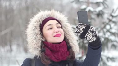 Genç güzel kız kendini onun smartphone cep telefonu ile bir kış parkta yürürken çekiyor.