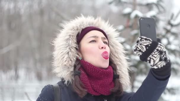 Ung vacker flicka tar bilder på sig själv på sin smartphone medan promenader i en winter park. — Stockvideo