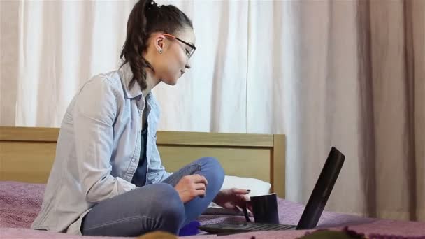 Una giovane bella ragazza che lavora dal suo computer portatile mentre beve caffè da una tazza nera . — Video Stock
