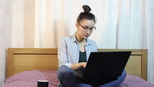 Una joven hermosa chica que trabaja desde su computadora portátil mientras bebe café de una taza negra . — Vídeos de Stock