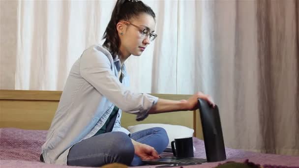 Una hermosa joven está abriendo su portátil y escribiendo en el teclado sentado en la cama . — Vídeo de stock