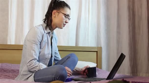 Молода красива дівчина працює з ноутбука, п'ючи каву з чорної чашки . — стокове відео