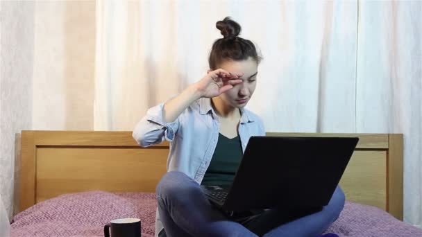 一个年轻美丽的女孩揉她的眼睛从疲劳工作在她的笔记本电脑上. — 图库视频影像