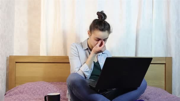 Ein junges schönes Mädchen reibt sich die Augen vor Müdigkeit bei der Arbeit an ihrem Laptop. — Stockvideo