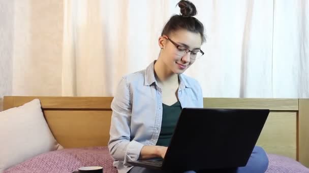 Młoda, atrakcyjna dziewczyna jest tekstylny wiadomość od swojego laptopa, siedząc na łóżku w domu. — Wideo stockowe