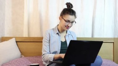Çekici bir kız evde yatakta oturmuş onu laptop üzerinde çalışıyor.