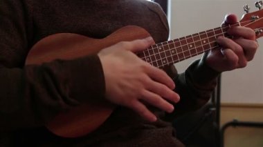 Genç bir adam ukulele oynarken elinde.