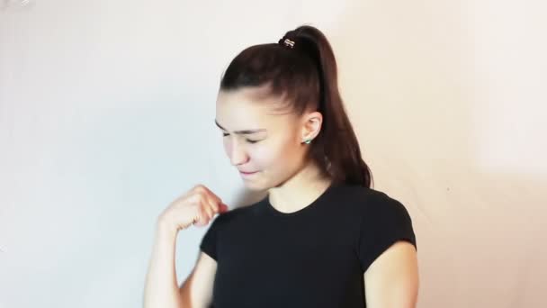 A beautiful young girl in a black t-shirt is smiling and showing thumb up looking at the camera. — Stock Video