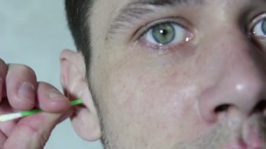 Young handsome guy cleans his ear with an ear stick.