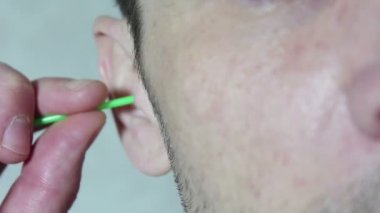 Young handsome guy cleans his ear with a cotton bud stick.