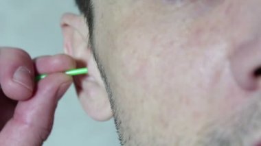 Young handsome guy cleans his ear with a cotton bud stick.