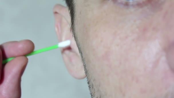 Młody przystojniak myje ucho kijem do uszu. — Wideo stockowe