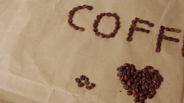 Η επιγραφή "καφές" και ένα σημάδι καρδιάς είναι από κόκκους καφέ σε χαρτί χειροτεχνίας. — Αρχείο Βίντεο