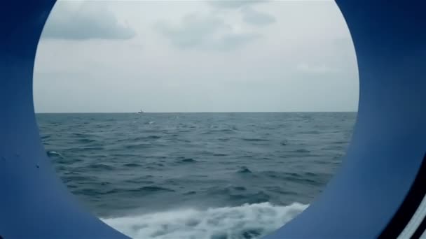 View of the ocean from the porthole of the ship going. A ship in the ocean is visible from the porthole of a cruise liner. — Stock Video