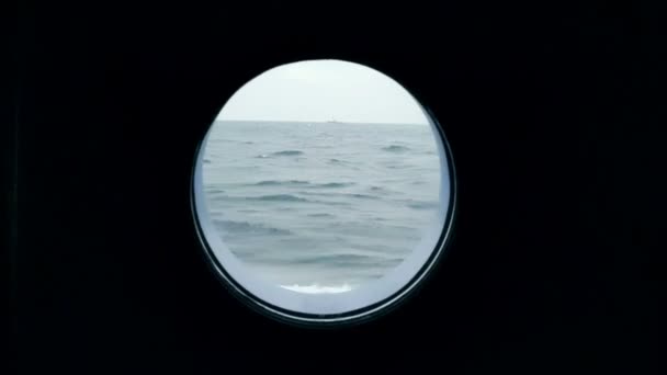 Uitzicht op de oceaan vanaf de patrijspoort van het schip gaat. Een schip in de Oceaan is zichtbaar vanuit de patrijspoort van een cruiseschip. — Stockvideo