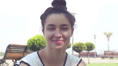 Yakın portre Beyaz bir t-shirt güzel genç kız kameraya bakar ve gülümseyerek. Güneşli bir yaz gününde parkta dinlenen güzel genç kız.