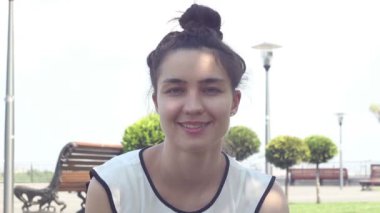 Yakın portre Beyaz bir t-shirt güzel genç kız kameraya bakar ve gülümseyerek. Güneşli bir yaz gününde parkta dinlenen güzel genç kız.