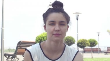 Yakın portre Beyaz bir t-shirt güzel genç kız kameraya bakar ve gülümseyerek. Güneşli bir yaz gününde parkta dinlenen güzel genç kız.