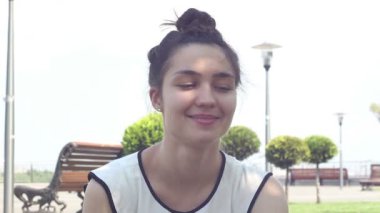 Yakın portre Beyaz bir t-shirt güzel genç kız kameraya bakar ve gülümseyerek. Güneşli bir yaz gününde parkta dinlenen güzel genç kız.