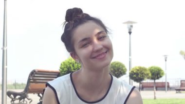 Yakın portre Beyaz bir t-shirt güzel genç kız kameraya bakar, gülümsüyor ve bir Hava öpücük gönderir. Güneşli bir yaz gününde parkta dinlenen güzel genç kız.