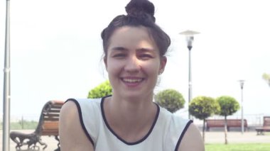 Yakın portre Beyaz bir t-shirt güzel genç kız kameraya bakar ve gülümseyerek. Güneşli bir yaz gününde parkta dinlenen güzel genç kız.