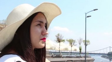 Yakın portre Beyaz şapkalı güzel bir genç kız kameraya bakar ve gülümser. Beyaz şapkalı genç ve çekici bir kız, bakışlarını gökyüzüne doğru kaldırıyor ve güneş ışınlarından gözlerini kısıyor..