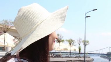 Yakın portre Beyaz şapkalı güzel bir genç kız kameraya bakar ve gülümser. Beyaz şapkalı genç ve çekici bir kız, bakışlarını gökyüzüne doğru kaldırıyor ve güneş ışınlarından gözlerini kısıyor..