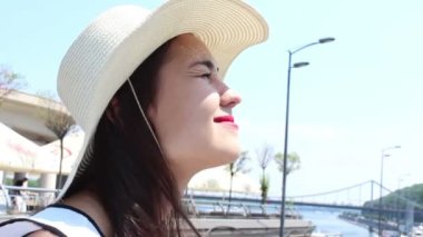 Beyaz şapkalı genç çekici kız, bakışlarını gökyüzüne doğru kaldırır ve güneşten gözlerini kısardı. Beyaz şapkalı güzel bir genç kızın portresini kapatın.