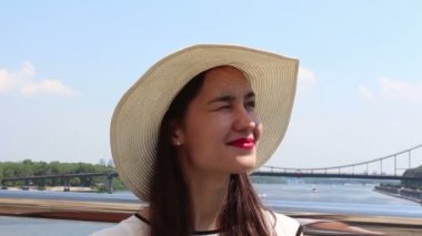 Beyaz şapkalı güzel bir genç kızın yakın portresi. Beyaz şapkalı genç çekici kız, bakışlarını gökyüzüne doğru kaldırıyor ve güneşten gözlerini kısıyor.