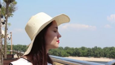 Yakın portre Beyaz şapkalı güzel bir genç kız kameraya bakar ve gülümser. Beyaz şapkalı genç ve çekici bir kız, bakışlarını gökyüzüne doğru kaldırıyor ve güneş ışınlarından gözlerini kısıyor..