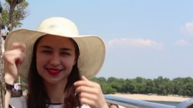 Yakın portre Beyaz şapkalı güzel bir genç kız kameraya bakar ve gülümser. Beyaz şapkalı genç ve çekici bir kız, bakışlarını gökyüzüne doğru kaldırıyor ve güneş ışınlarından gözlerini kısıyor..