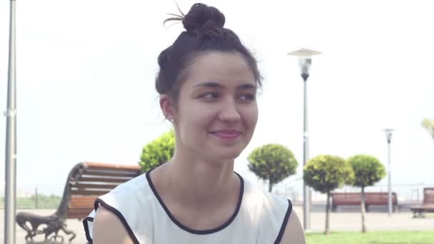 Retrato de cerca Hermosa joven con una camiseta blanca mira a la cámara y sonríe . — Vídeos de Stock