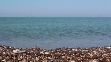 Deniz ve kayalık kıyı manzarası, deniz çakıl taşları ile. Berrak mavi suyla deniz. Kayalık sahilde deniz sörfü.