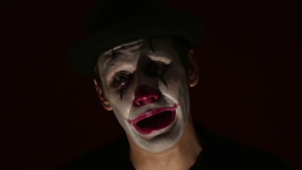 Scary man in a clown makeup looks at the camera and laughs. A scary clown looks at the camera and laughs terribly.Scary clown grimaces looking into camera .Halloween. — Stock Video