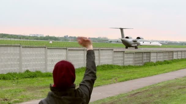 Una joven saludando siguiendo un avión militar que sale . — Vídeo de stock