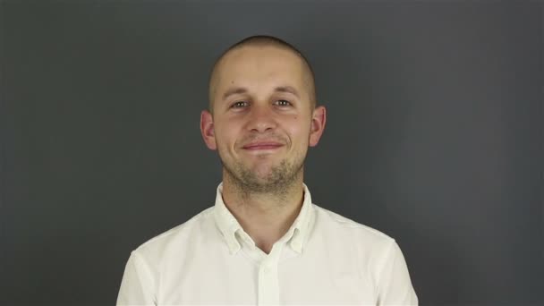 Ett närbild porträtt av en ung attraktiv kille, han tittar på kameran och ler. Porträtt på en grå bakgrund. — Stockvideo