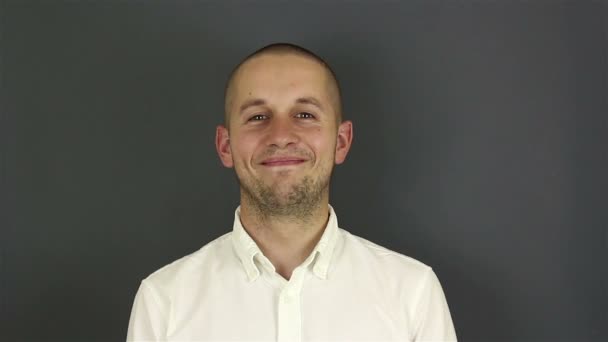 Un retrato de cerca de un joven atractivo, él está mirando a la cámara y sonriendo. Retrato sobre fondo gris . — Vídeos de Stock