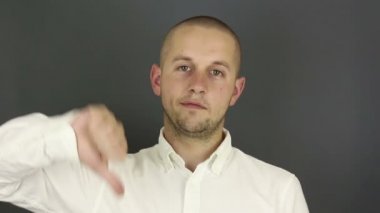 Komik yakışıklı adam onaylamadığını belirterek baş parmağını kaldırdı. Gri arkaplanda bir portre.