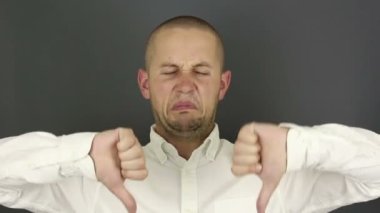 Komik yakışıklı adam onaylamadığını belirterek baş parmağını kaldırdı. Gri arkaplanda bir portre.